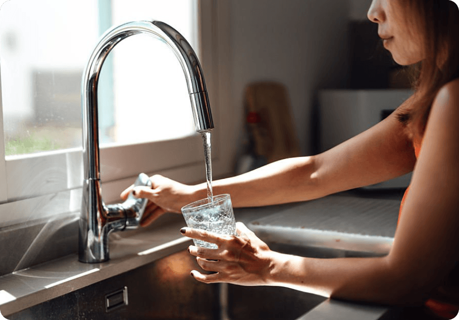 Woman filling a glass of water from a kitchen tap.